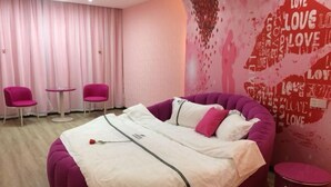 A bedroom with a large bed, two pink chairs, a small table, and a wall with 'LOVE' text. - Junyi Chain Hotel (Tianmen baoan palza Store) (Tianmen)