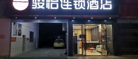 A hotel entrance with a sign in Chinese characters, a reception desk, and a car parked outside.