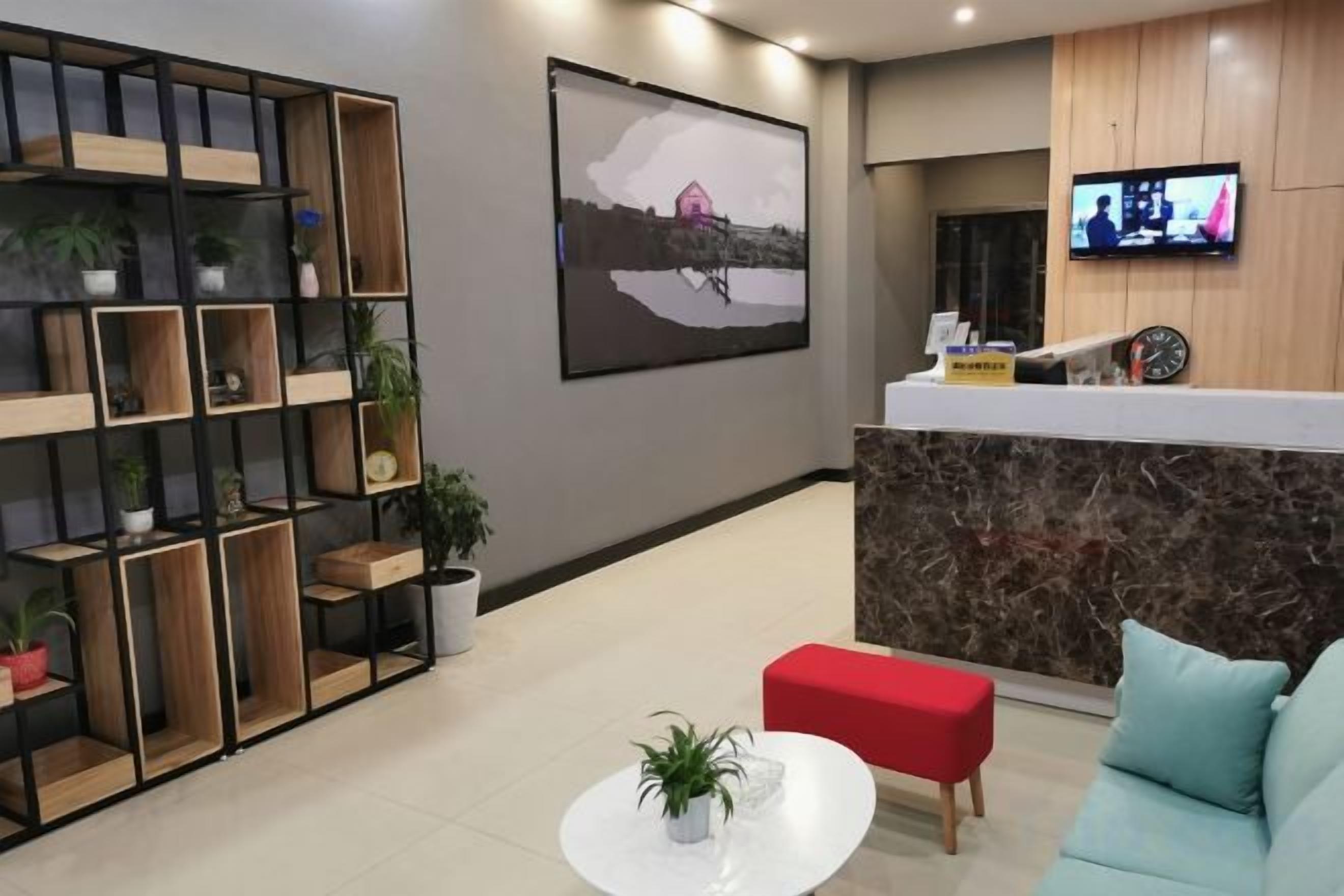 A reception area with a reception desk, a television, a wall-mounted clock, and a seating area with a red ottoman and a blue sofa.
