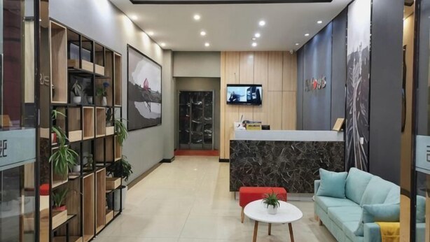 A modern hotel lobby with a reception desk, a TV, a sofa, a coffee table, and a plant display. - Junyi Chain Hotel (Tianmen baoan palza Store) (Tianmen)