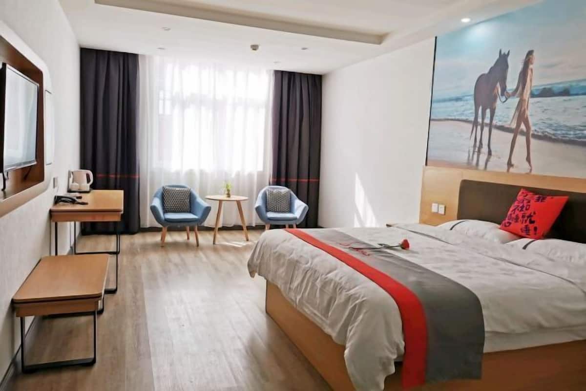 A hotel room with a bed, a desk, two chairs, a small table, and a painting on the wall.