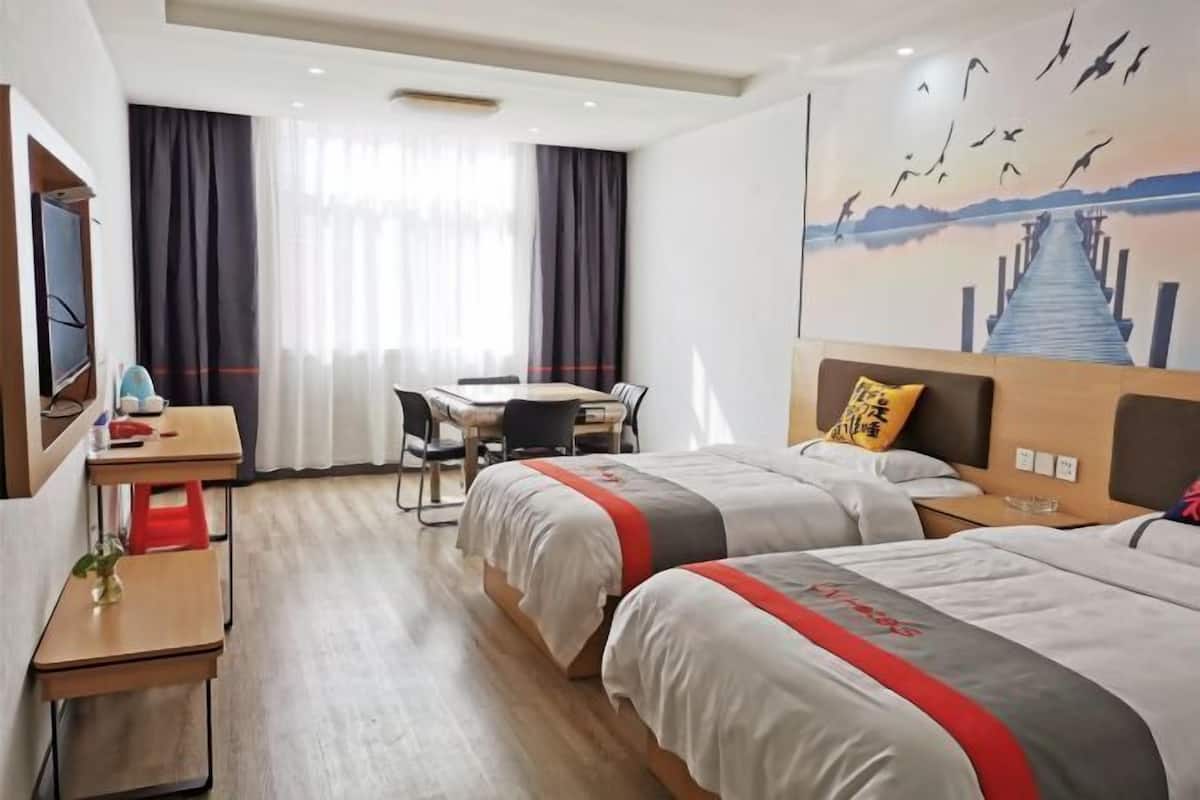 A hotel room with two beds, a desk, a chair, a TV, and a painting of birds on a pier.