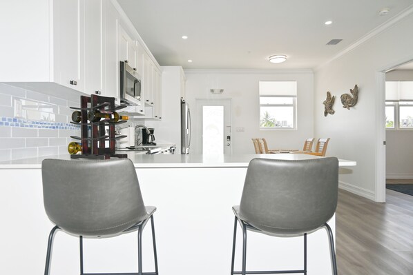 Une cuisine moderne avec des meubles blancs, un réfrigérateur en acier inoxydable et un coin repas comprenant une table blanche et des chaises grises.