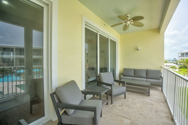 A balcony with grey furniture, a ceiling fan, and a view of a swimming pool and buildings. - *New Luxury Beachfront* Kokomo Views Beach,Pool (Key Colony Beach)
