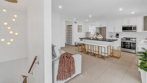 A modern kitchen with white cabinets, a central island with stools, stainless steel appliances, and a hanging light fixture. - *NEW* Casa Coco-Pool/Tennis/Ramp (Key Largo)