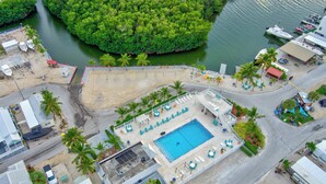 An aerial view of a resort with a swimming pool, beach area, and boats docked near a forested island. - *NEW* Casa Coco-Pool/Tennis/Ramp (Key Largo)
