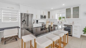 A modern kitchen with white cabinetry, stainless steel appliances, a marble island with bar stools, and a large window providing natural light. - *NEW* Casa Coco-Pool/Tennis/Ramp (Key Largo)