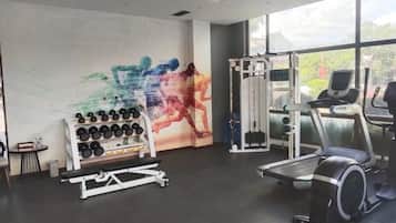 A gym with exercise equipment, a wall with a colorful abstract painting, and a window with a view of greenery.