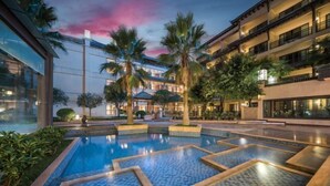 Une cour d’hôtel avec une piscine, des palmiers et un ciel au coucher du soleil.