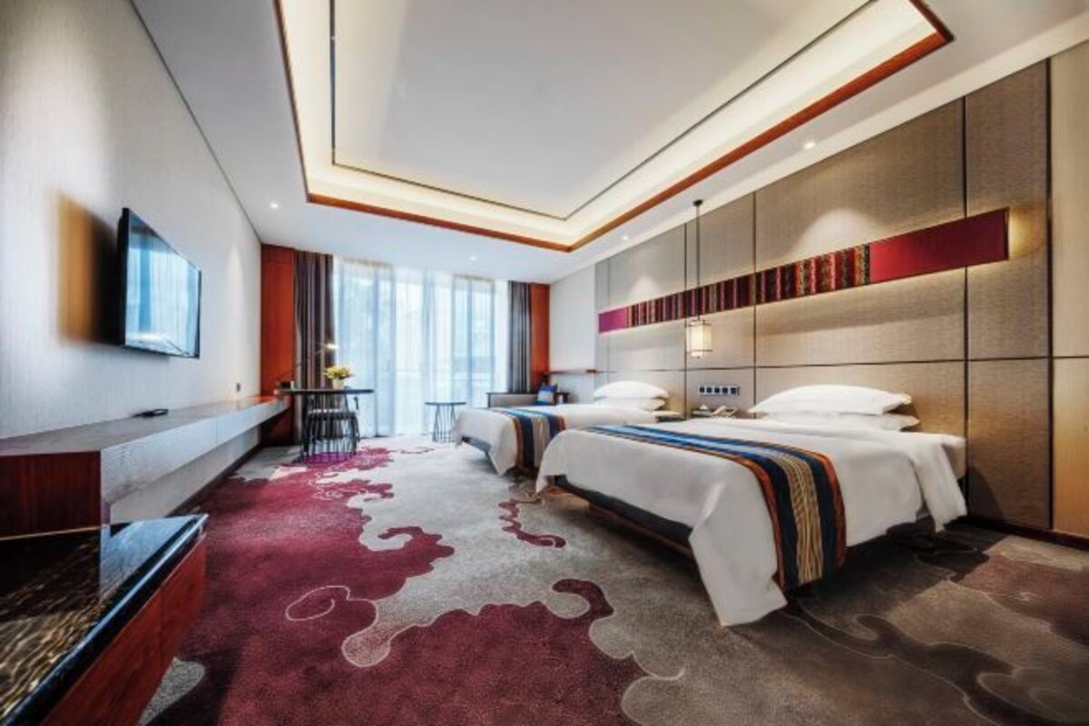 A modern hotel room with two beds, a desk, a TV, and a large window.