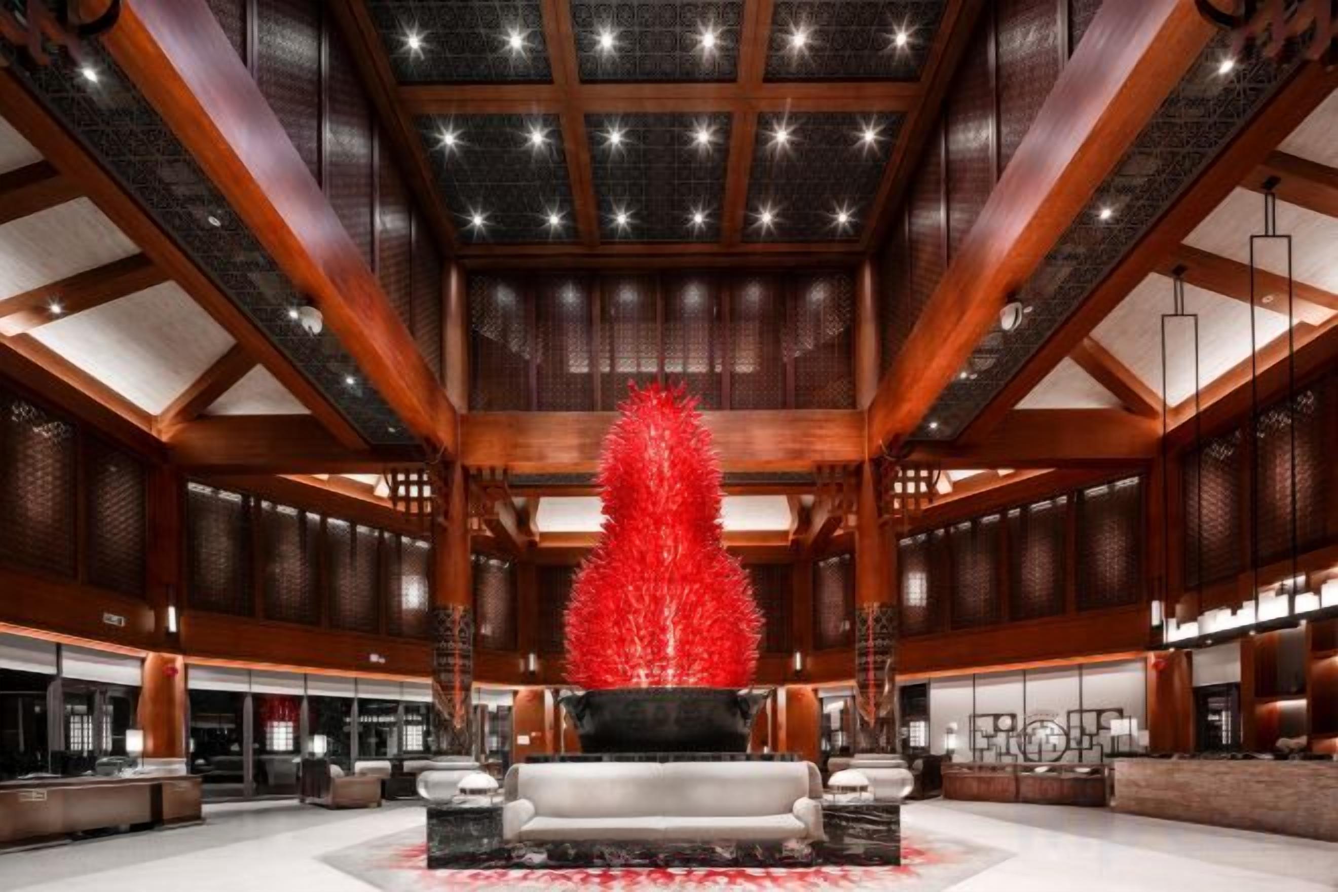 Un vestíbulo amplio con una zona de estar central, techos altos con vigas de madera y un elemento decorativo rojo grande.