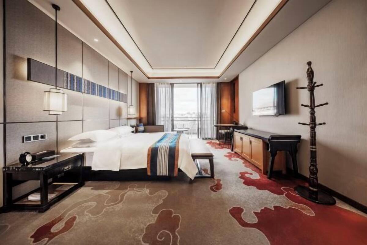 Ein modernes Hotelzimmer mit einem großen Bett, Nachttischen, einem Schreibtisch, einem Fernseher und Blick auf die Stadt.