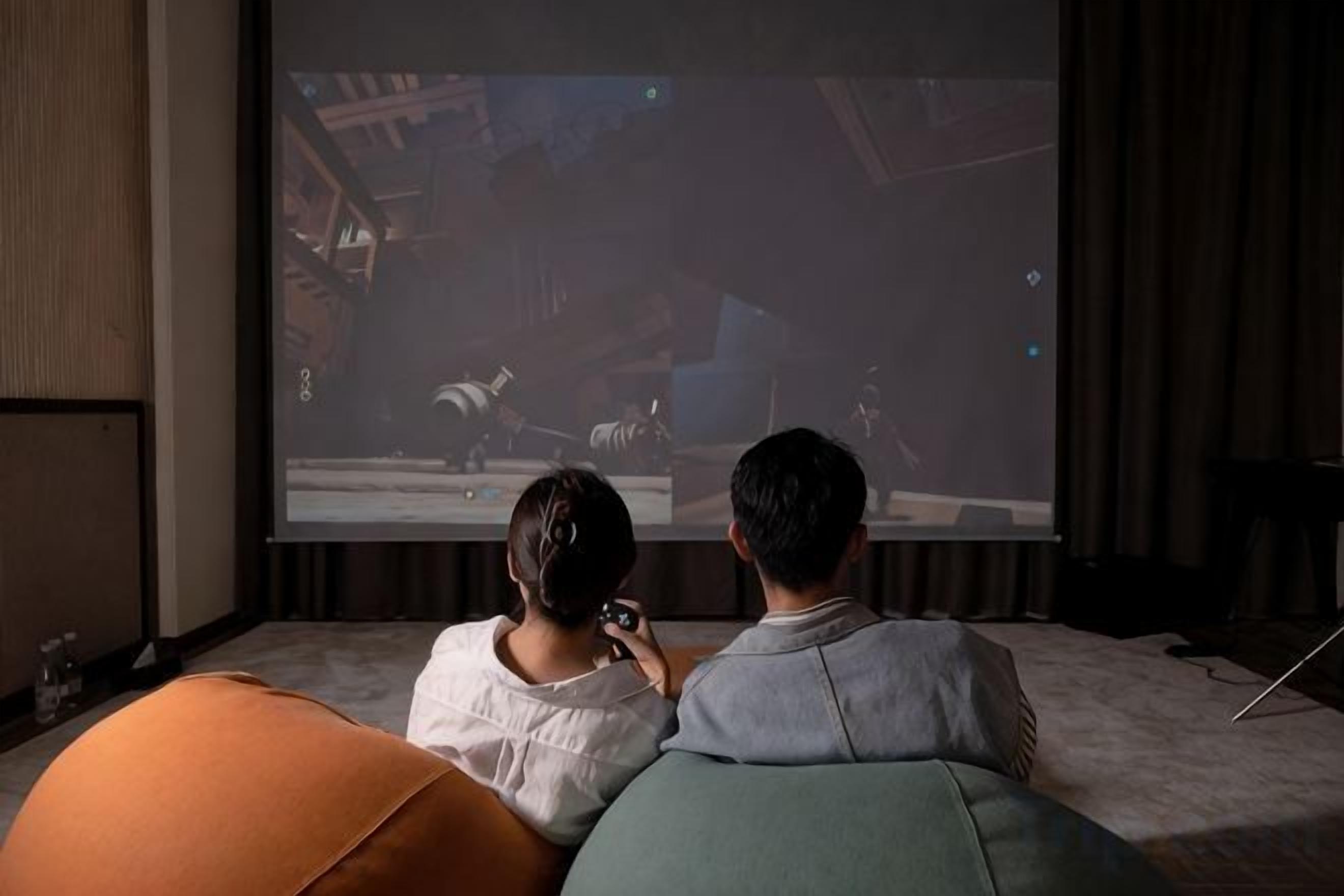 Duas pessoas sentadas num sofá assistindo a um filme numa tela grande.