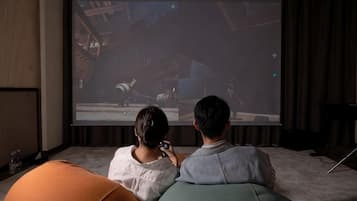 Duas pessoas sentadas num sofá assistindo a um filme numa tela grande.
