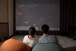 Duas pessoas sentadas num sofá assistindo a um filme numa tela grande.