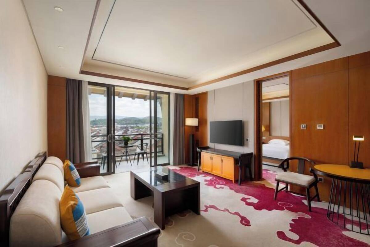 Ein Hotelzimmer mit einer Couch, einem Fernseher, einem Esstisch und Blick auf die Stadt.