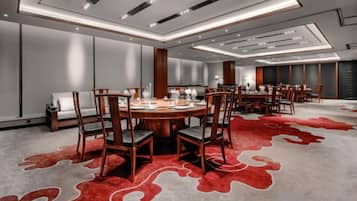 Un salón de conferencias con una mesa redonda, sillas y una alfombra con un diseño abstracto rojo.