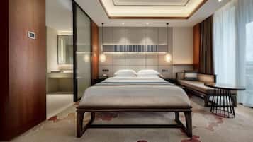 Una habitación de hotel moderna con una cama grande, un área de descanso con un sofá y una pequeña mesa, y un ventanal con cortinas.