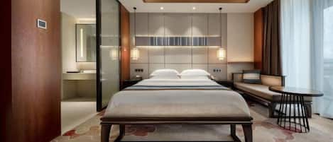 Une chambre d’hôtel moderne dotée d’un grand lit, d’un coin salon avec un canapé et une petite table, ainsi que d’une grande fenêtre avec des rideaux.