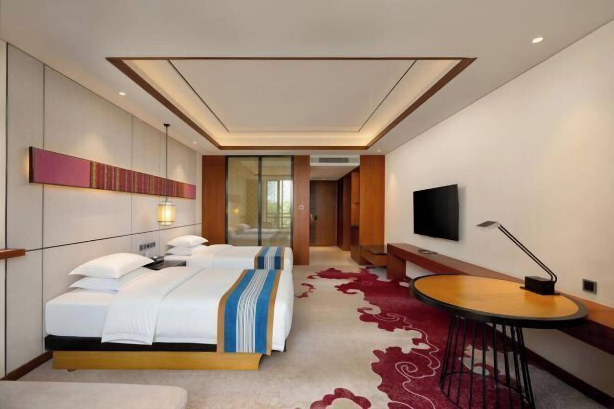 Ein Hotelzimmer mit Bett, Nachttisch, Fernseher und einem roten Teppich.