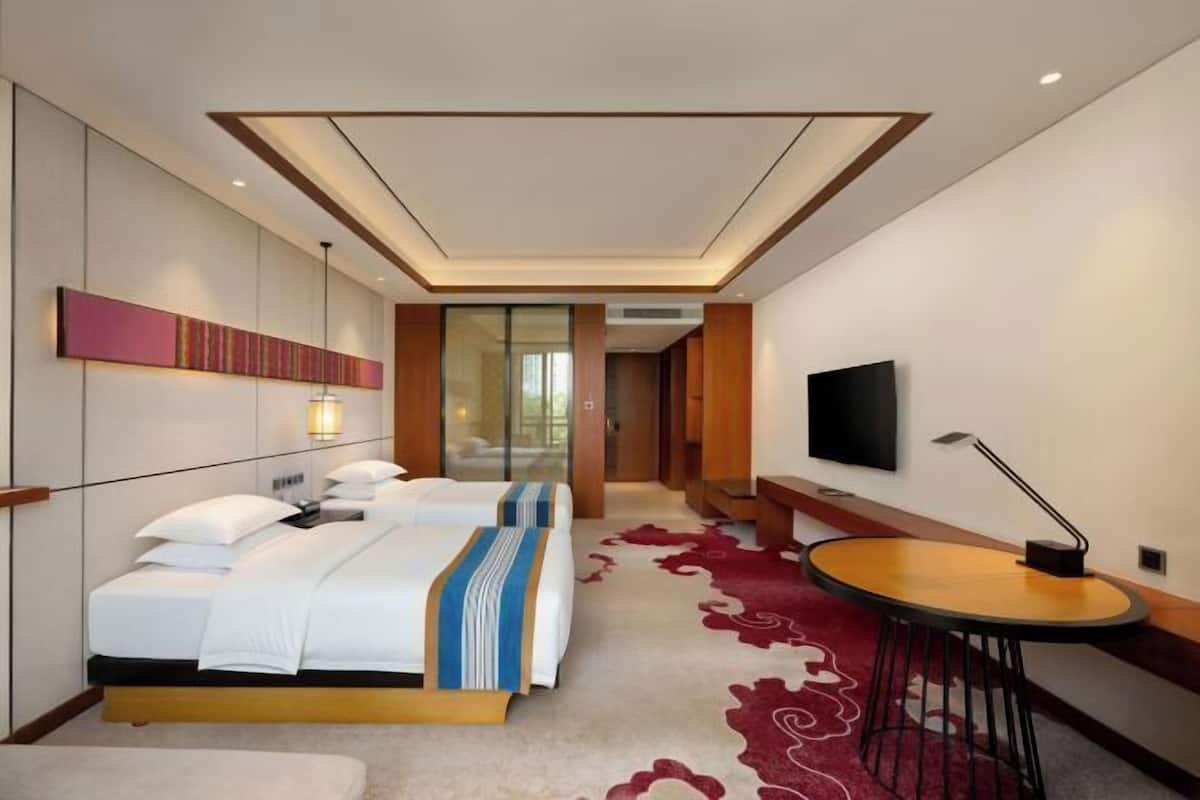 A hotel room with a bed, bedside table, TV, and a red carpet.