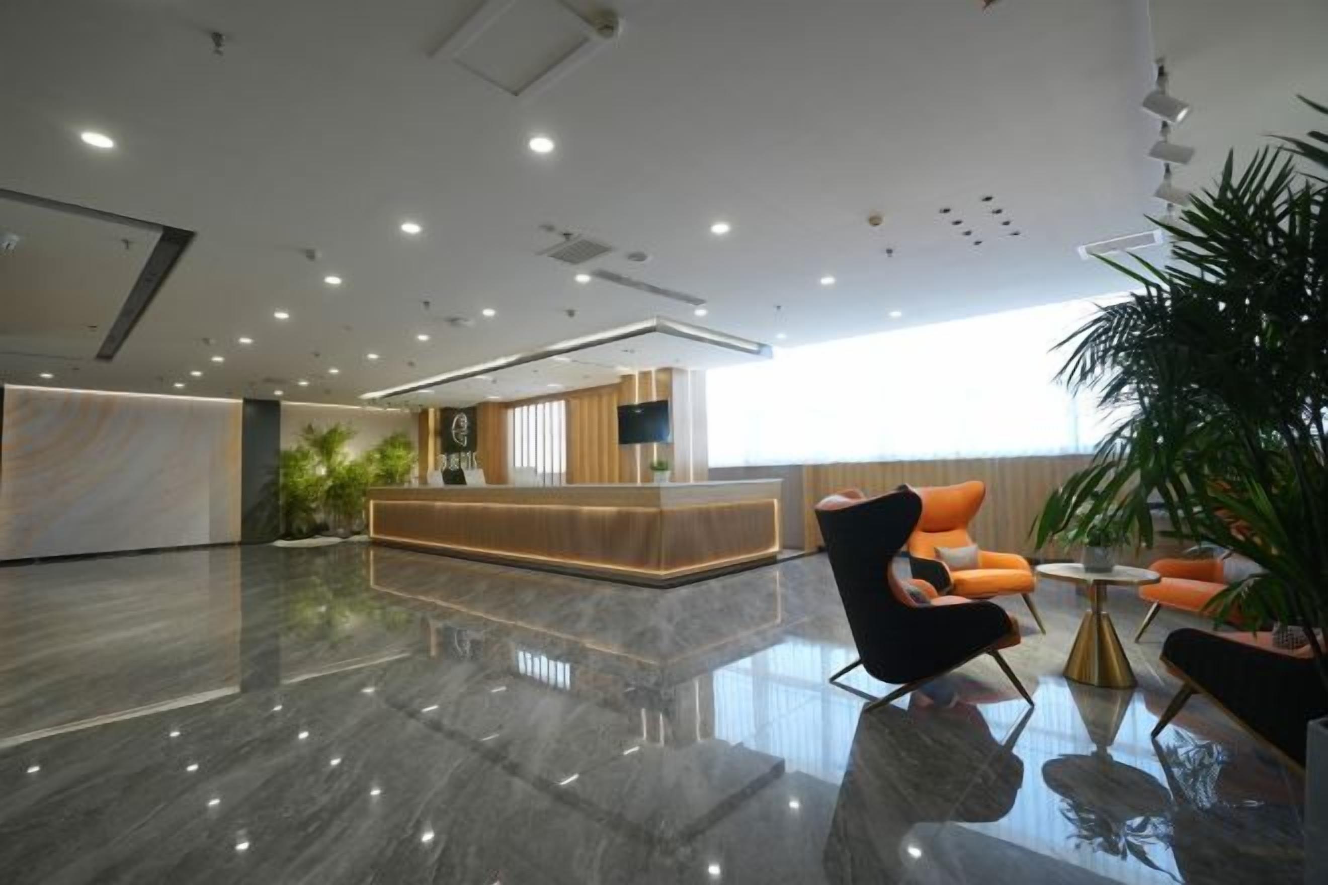 A modern hotel lobby with a reception desk, seating area, and a large window providing natural light.