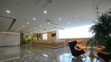 A modern hotel lobby with a reception desk, seating area, and a large window providing natural light.