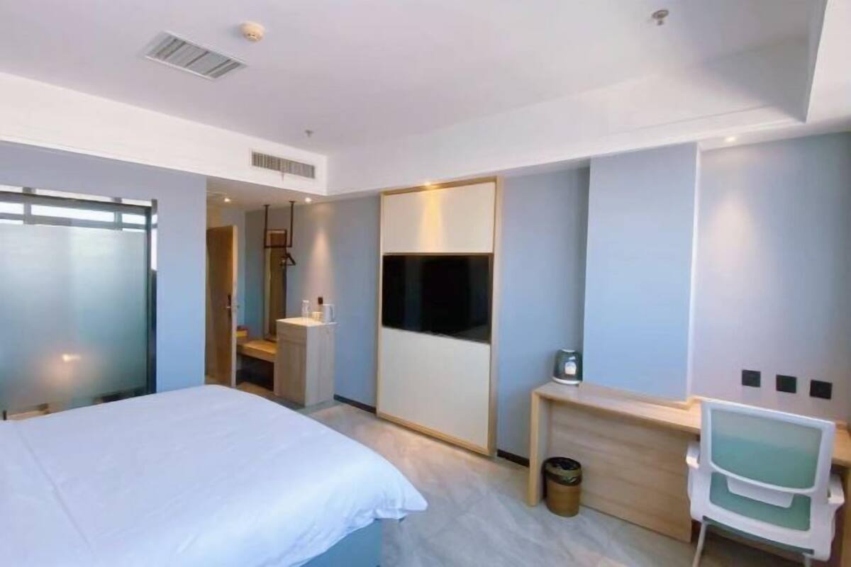 Quarto de hotel moderno com cama, escrivaninha, cadeira, espelho e televisão.