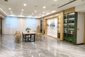 A spacious room with a marble floor, a wooden table with chairs, a large window with curtains, and a bookshelf with decorative items. - Tianjing Hotel (Shenyang)