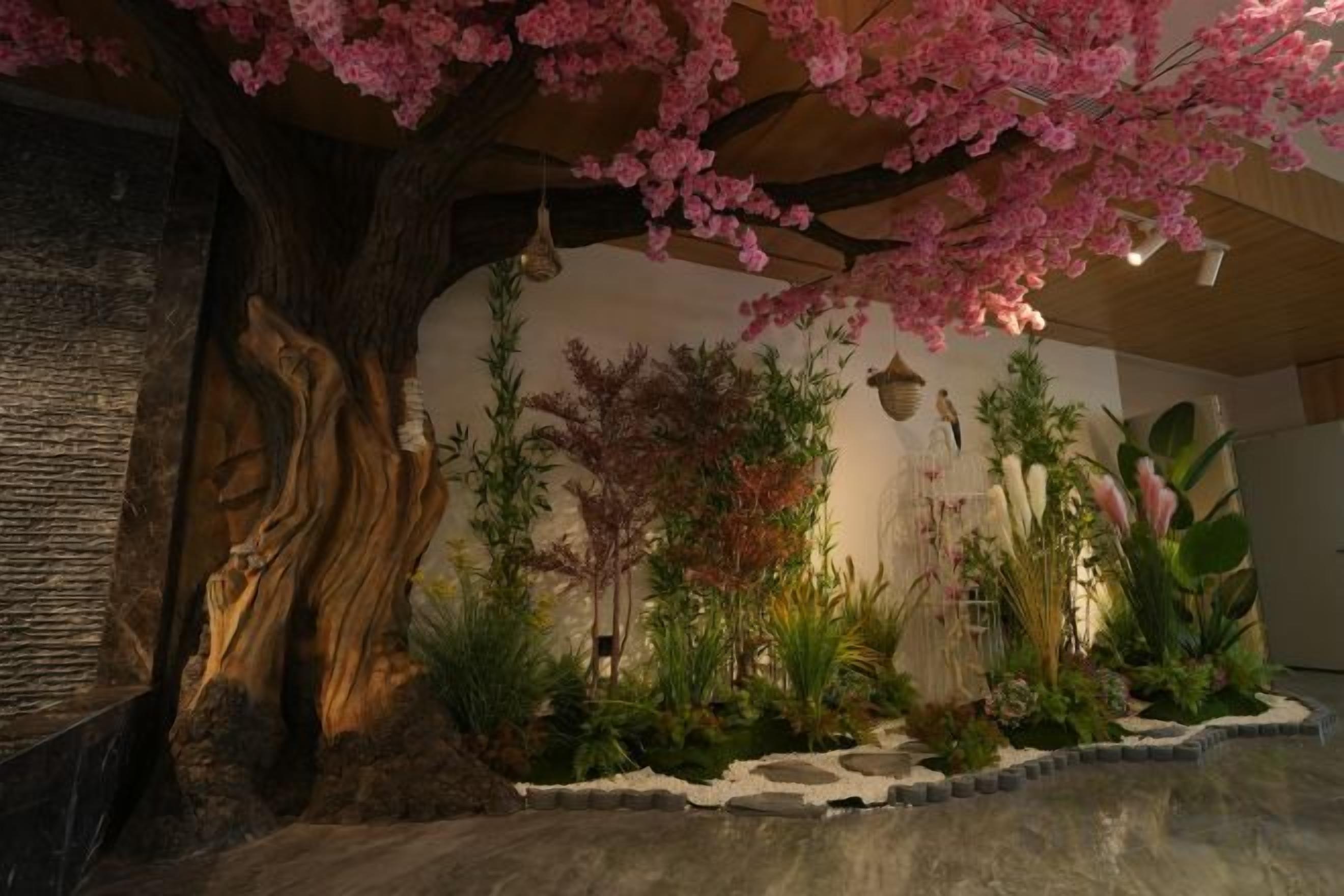 A room with a large tree, a rock formation, and various plants.