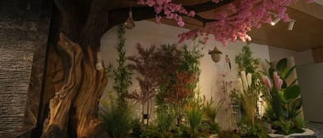 A room with a large tree, a rock formation, and various plants.