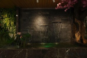 A dark stone wall with a water feature and a wooden sculpture. - Tianjing Hotel (Shenyang)
