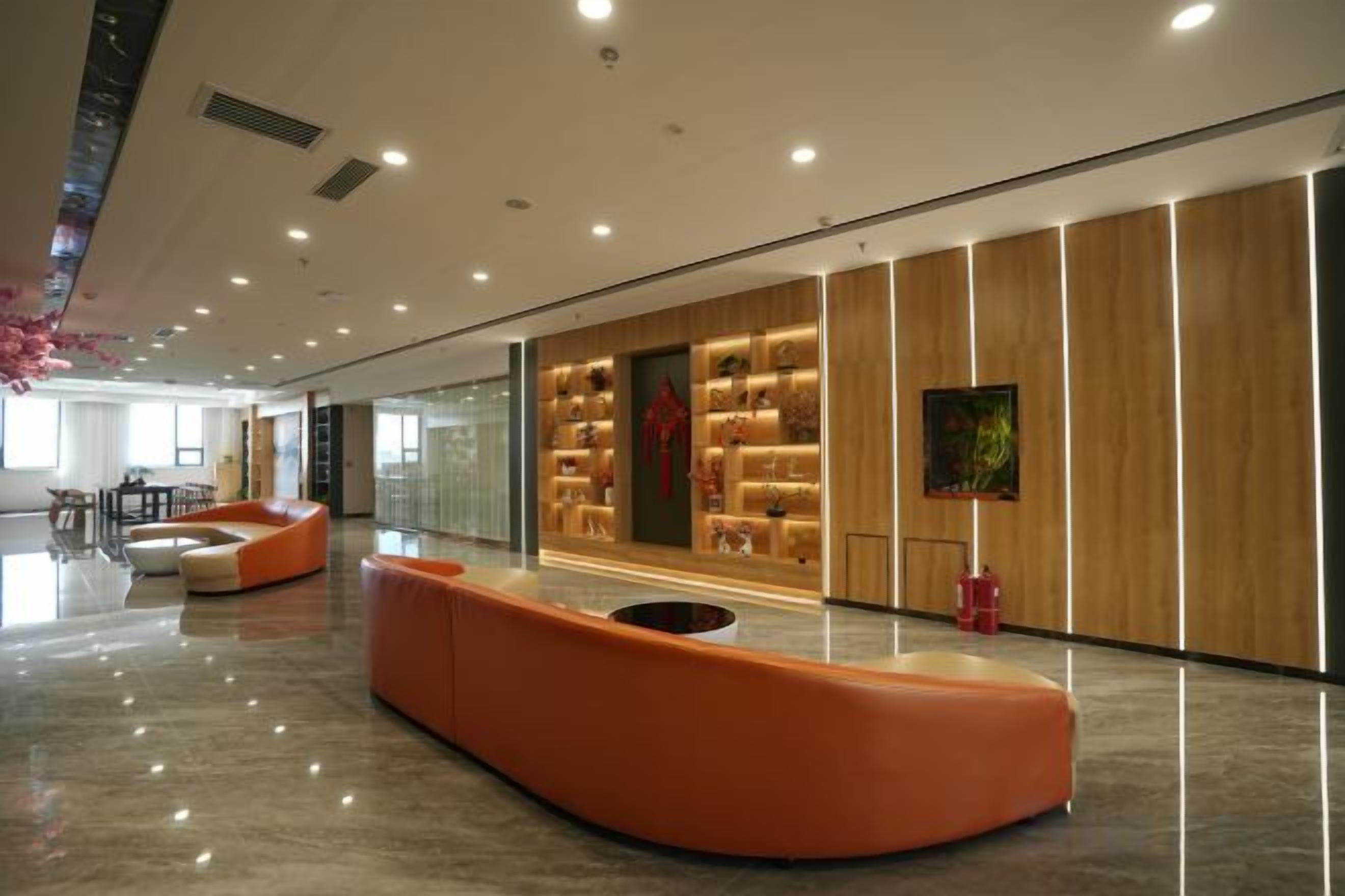 A modern lobby with a curved orange seating area, a wooden wall with display cabinets, and a large painting.