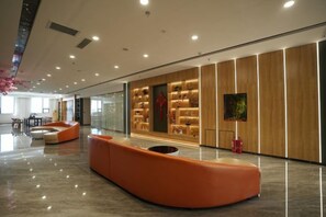 A modern lobby with a curved orange seating area, a wooden wall with display cabinets, and a large painting. - Tianjing Hotel (Shenyang)