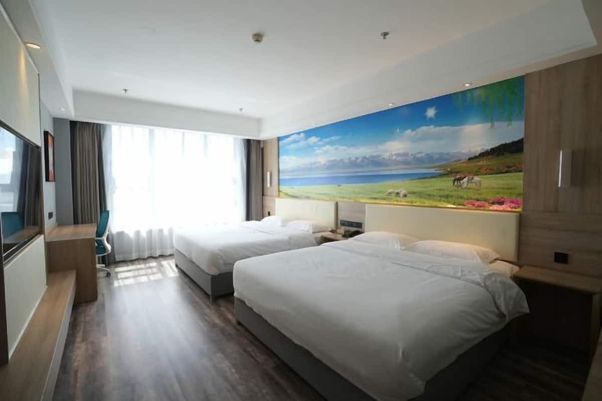 Quarto de hotel com duas camas, uma escrivaninha e uma janela grande com cortinas.