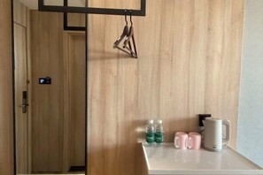A hotel room with a wooden wall, a white countertop, and a hanging light fixture. There are two bottles of water and two pink mugs on the counter. - Tianjing Hotel (Shenyang)