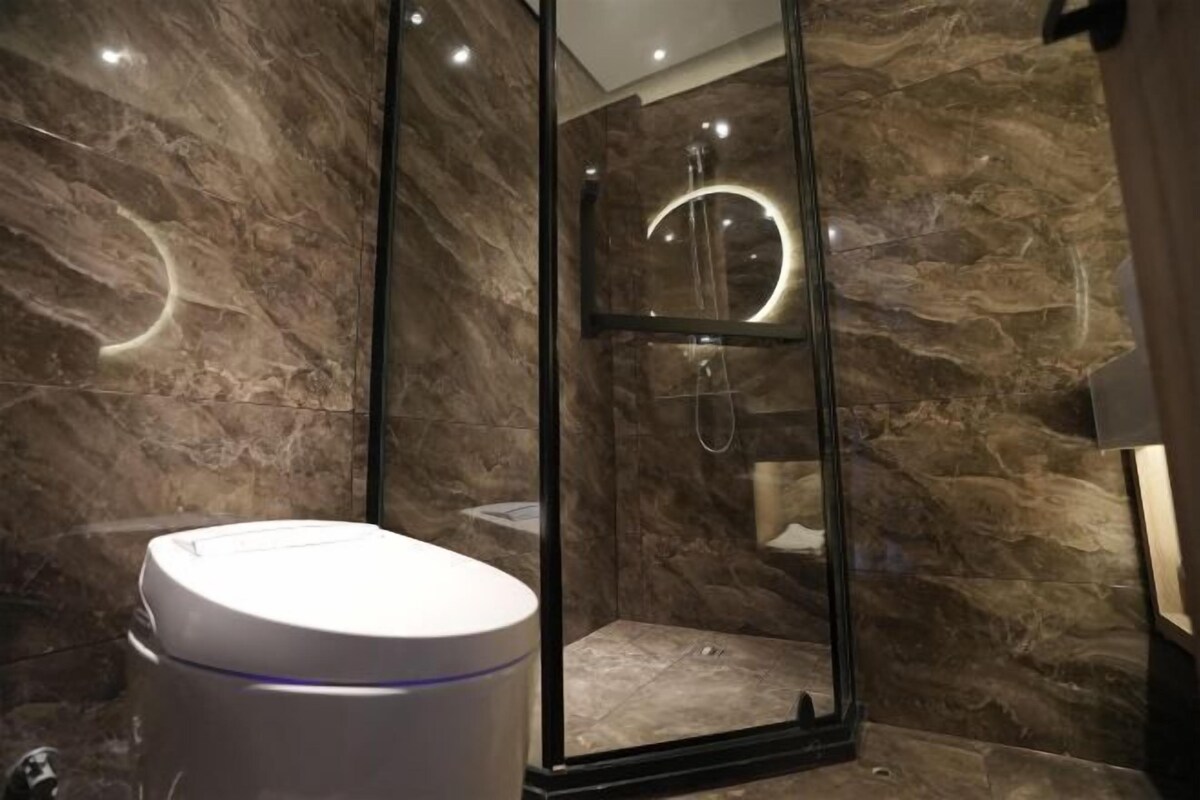 A modern bathroom with a glass-enclosed shower, a white toilet, and marble walls.