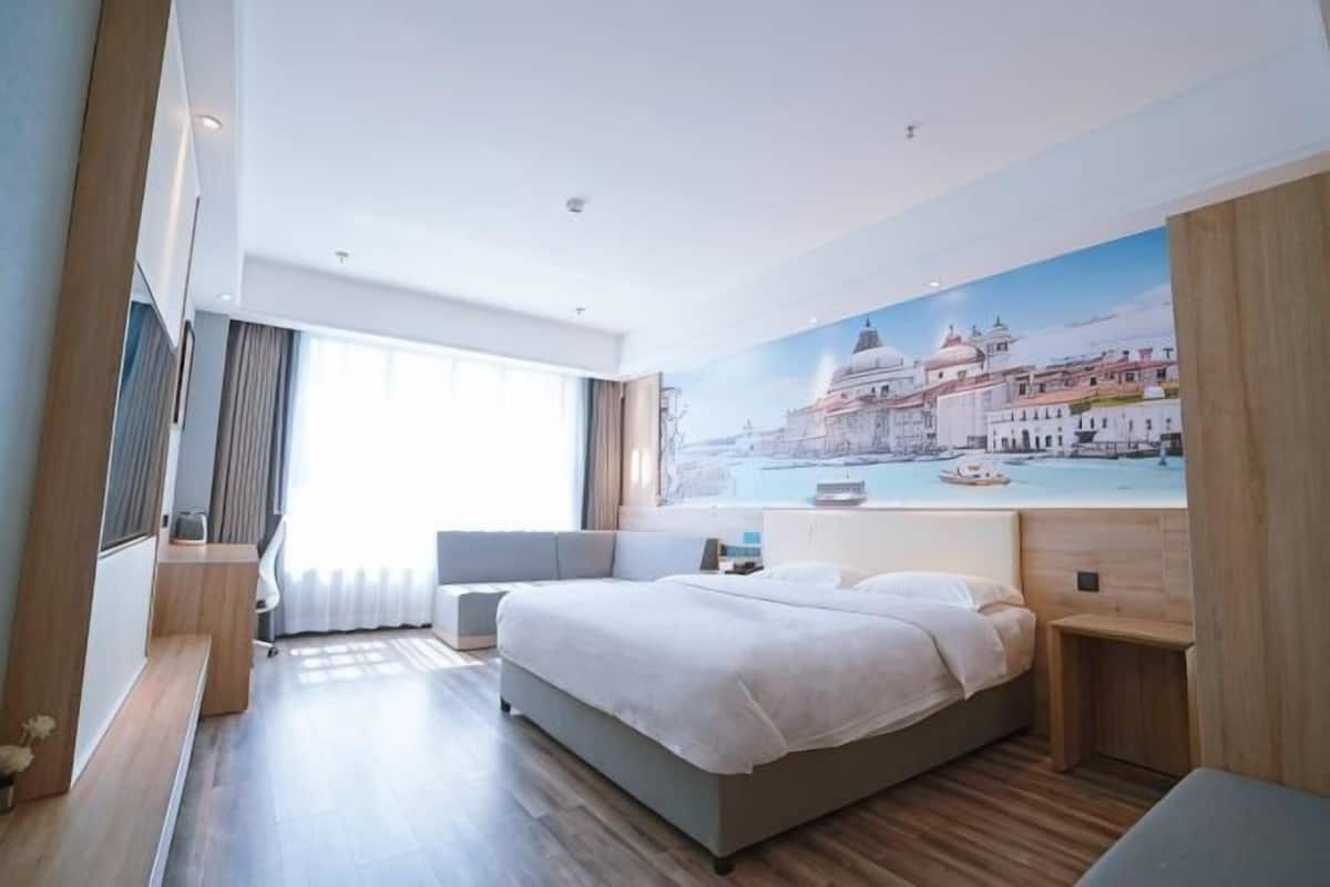 Quarto de hotel moderno com uma cama grande, um espaço de estar, uma pintura de paisagem urbana e uma janela ampla.