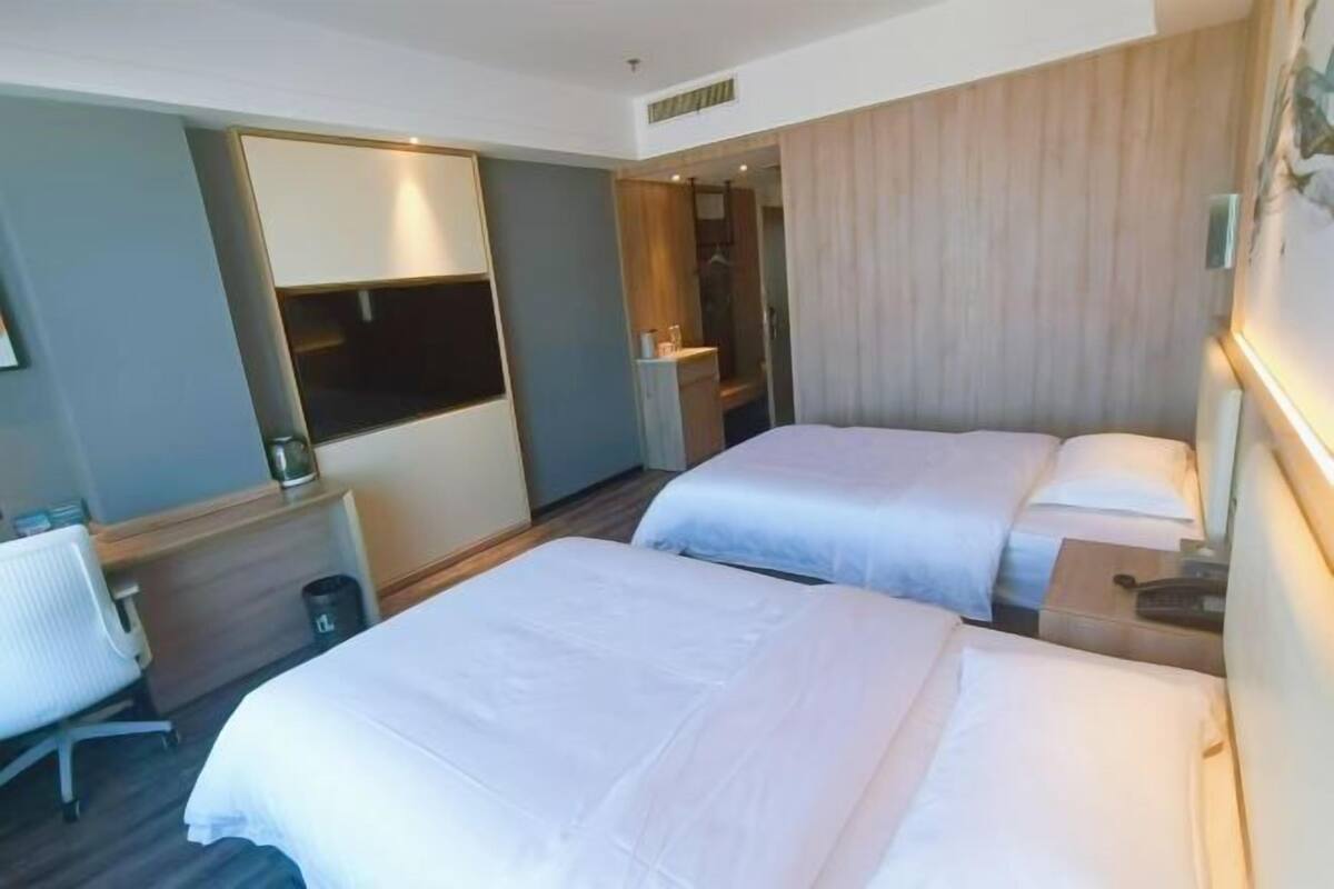 Quarto de hotel com duas camas, uma escrivaninha e um espelho.
