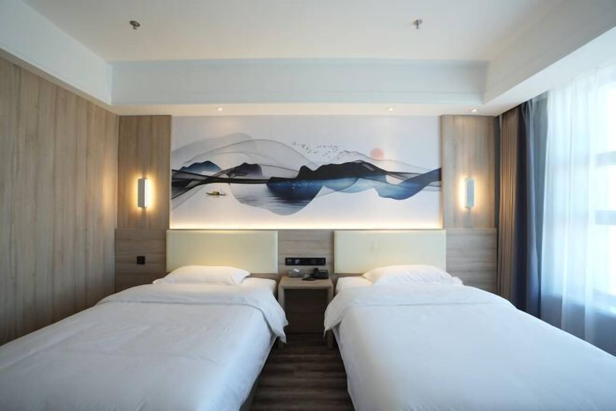Quarto de hotel com duas camas, um mural grande na parede e uma mesa de cabeceira com abajur.