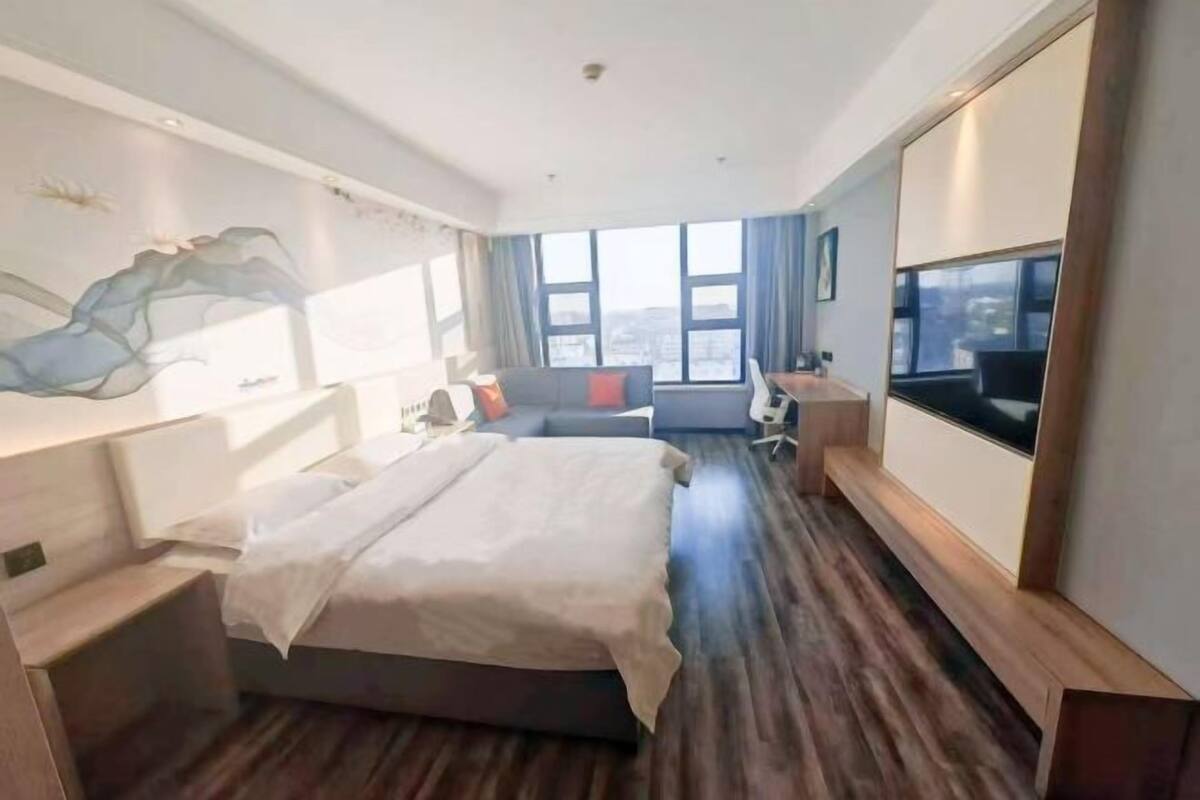 Quarto de hotel moderno com uma cama grande, uma escrivaninha, uma cadeira, uma TV e uma janela ampla com vista para a cidade.