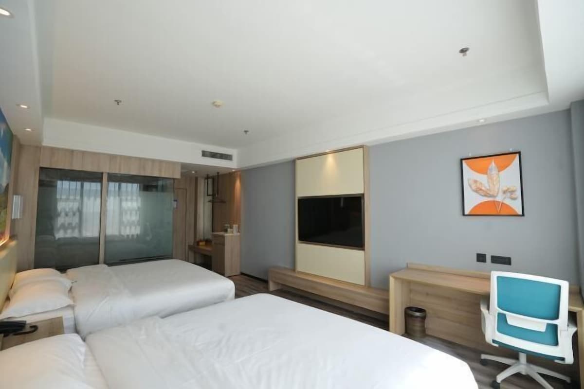 A hotel room with two beds, a desk, a chair, a TV, and a large mirror.