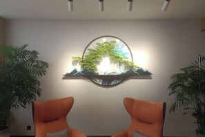 A room with two orange chairs, a wall-mounted shelf with a circular mirror, and two potted plants. - Tianjing Hotel (Shenyang)