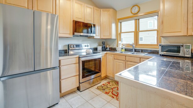 A kitchen with wooden cabinets, stainless steel appliances, a microwave, and a clock on the wall.