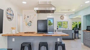Eine moderne Küche mit einer Holzinsel, schwarzen Barhocker, einer Edelstahl-Dunstabzugshaube und einem Kühlschrank.