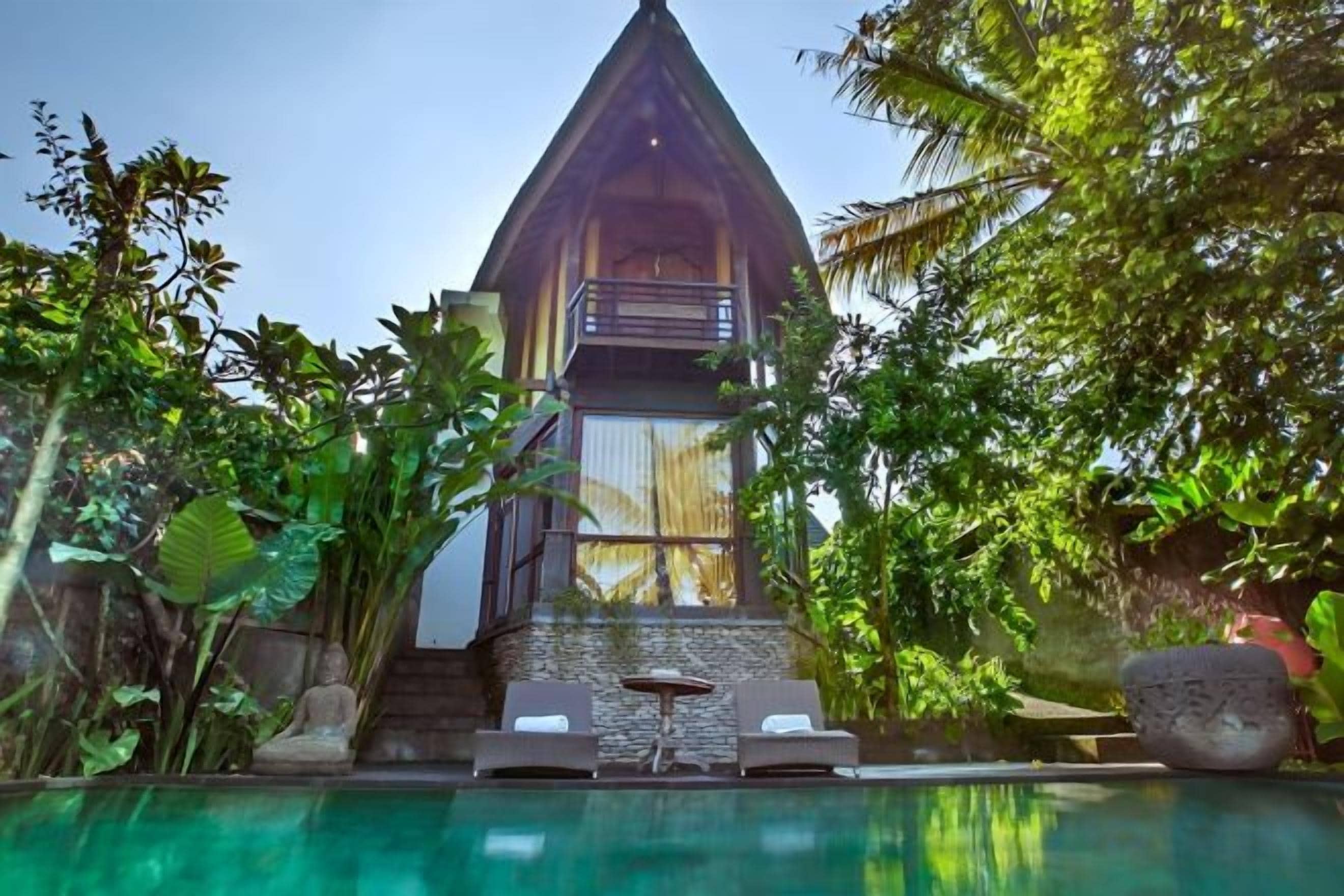 A modern building with a triangular roof, surrounded by lush greenery and a clear pool.