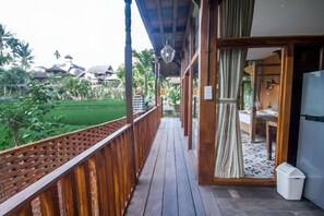 A wooden balcony with a view of a green landscape and a building in the background. - Gusde House and Villa Bali (Bali)