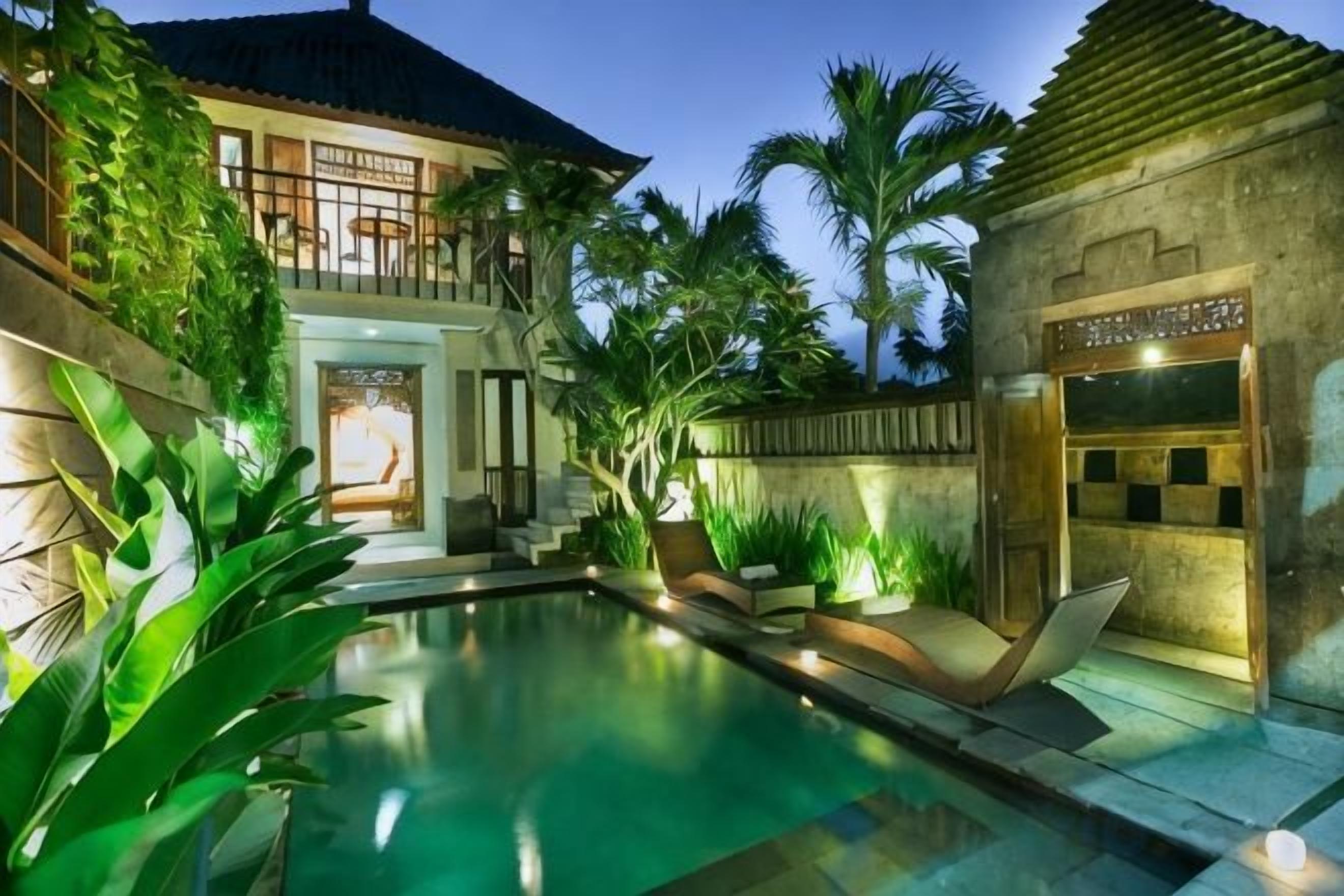 Une piscine avec un espace de détente, un bâtiment doté d’un balcon et une petite construction à motifs à carreaux.
