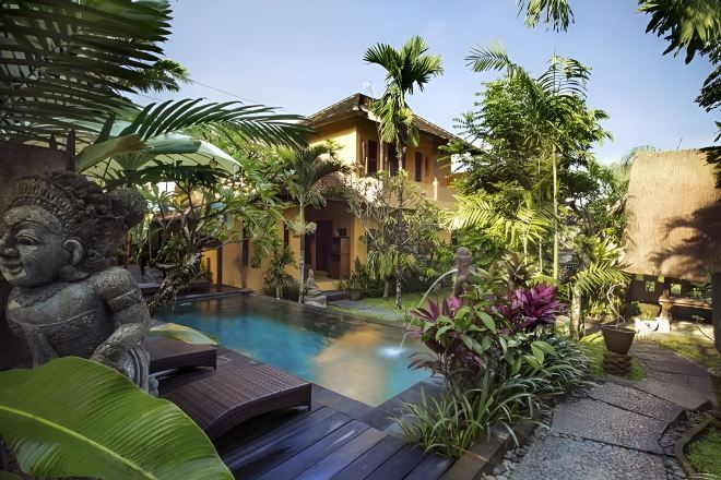 A pool area with a thatched-roof building, surrounded by tropical plants and a statue.