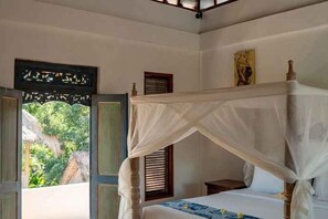 A room with a four-poster bed, a small table, and a window with blinds. - Gusde House and Villa Bali (Bali)